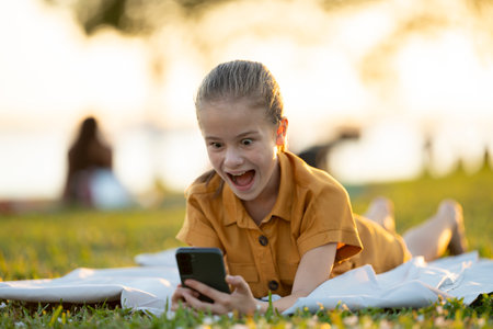 Happy pretty child girl browsing social media on her cellphone in summer parkの写真素材