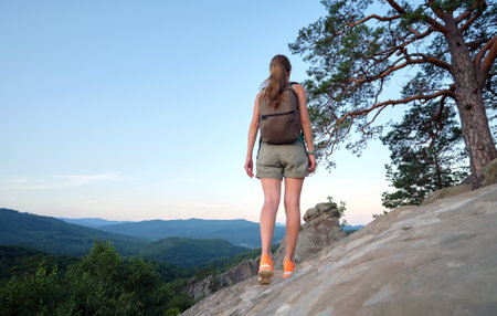 Hiker woman walking on mountain footpath enjoying evening nature. Lonely female traveler traversing wilderness trail. Healthy lifestyle conceptの写真素材