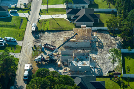 Lifting crane truck and builders working on roof construction of unfinished residential house with wooden frame structure in Florida suburban area. Housing development conceptの写真素材