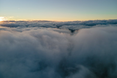 Aerial view from airplane window at high altitude of dense puffy cumulus clouds flying in eveningの写真素材
