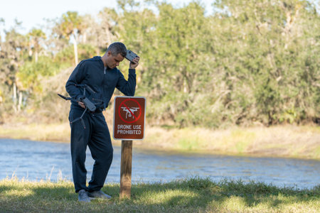 Man is sad that he is not allowed to fly his quadcopter state park no drone area. Operator is unauthorised to use UAS near restriction signの写真素材
