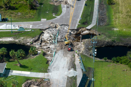 Repair of destroyed bridge after hurricane flood in Florida. Reconstruction of damaged road after flooding water washed away asphalt. Construction equipment at roadwork siteの写真素材