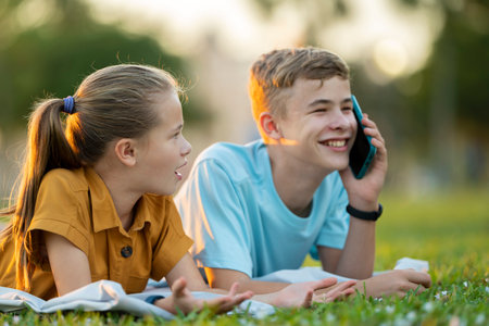 Sad teen friend being ignored by another outdoors while he is talking happily on mobile phone and paying no attention. Friendship problems conceptの写真素材