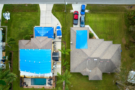 Hurricane Ian damaged house rooftop covered with protective plastic tarp against rain water leaking until replacement of asphalt shingles. Aftermath of natural disasterの写真素材