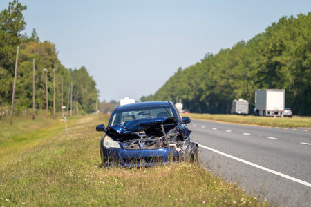 Old crashed car abandoned on highway road shoulder. Damaged in traffic accident vehicle parked on roadsideの写真素材