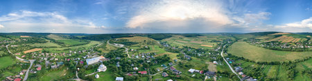 Aerial landscape view of village houses and distant green cultivated agricultural fields with...