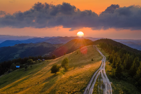 Amazing mountain landscape. Bright colorful sunset in wild national park highlands. Dark dirt road winding on hilltop illuminated with yellow setting sunの写真素材