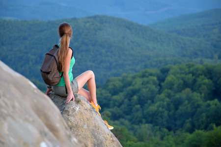 Young woman hiker sitting alone on rocky mountain enjoying view of summer nature on wilderness trail. Active way of life conceptの写真素材
