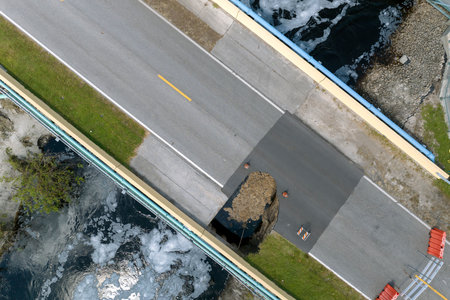 Roadworks site. Reconstruction of damaged road bridge destroyed by river after flood water washed away asphalt. Rebuilding of ruined transportation infrastructureの写真素材