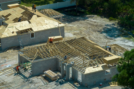 Aerial view of builders working on unfinished residential house with wooden roof frame structure...