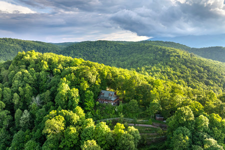 House on mountain side and lush forest illuminated with bright setting sun in North Carolina Appalachian mountains. Aerial view of colorful sunset in wild mountains. Beautiful nature landscapeの写真素材