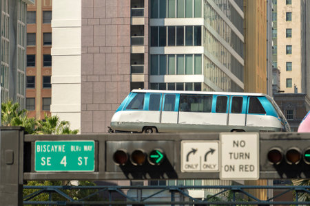 Urban transportation in downtown district of Miami Brickell in Florida USA. Metrorail city train car on high railroad over street traffic between skyscraper buildings in modern American megapolisの写真素材