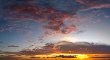 Colorful sunset sky with setting sun behind vivid orange and yellow cloudsの写真素材
