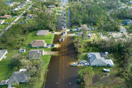 Flooded Florida road with evacuating cars and surrounded with water houses in suburban residential area. Consequences of hurricane natural disasterの写真素材