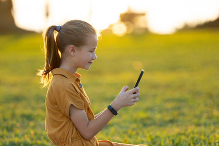 Happy teenage girl messaging on her cellphone outdoors sitting in summer parkの写真素材