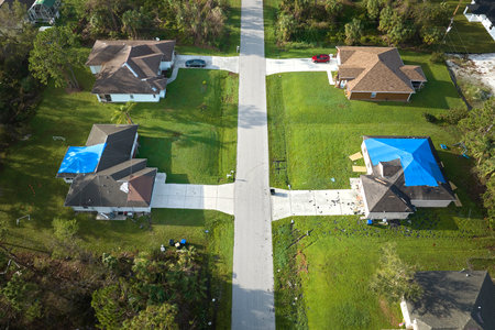 Hurricane Ian damaged house rooftops covered with protective plastic tarp against rain water leaking until replacement of asphalt shingles. Aftermath of natural disasterの写真素材