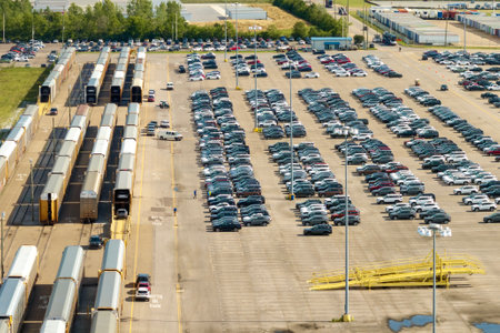 Industrial cargo trains at automotive factory loaded with new cars ready for transporting. Automaker parking lot with vehicles for saleの写真素材