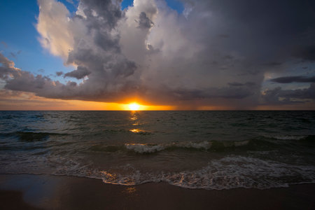 Dark clouds at sunset over evening sea water waves crushing on sandy beach. Seascape weather at sunsetの写真素材