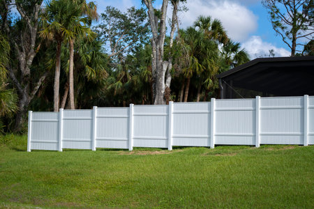 White vinyl picket fence on green lawn surrounding property grounds for backyard protection and privacyの写真素材