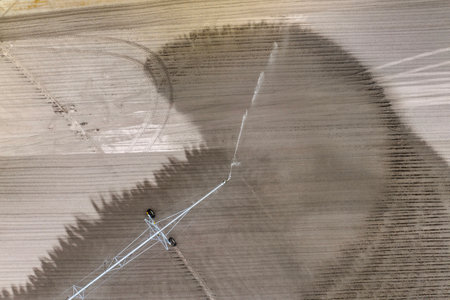 Agricultural irrigation sprinkler watering dry soil on farm field for crops growing during period of droughtの写真素材