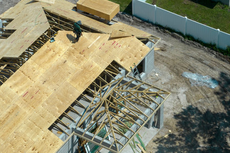 Professional builders working on roof construction of unfinished suburban home with wooden frame structure in Florida rural area. Concept of housing development in Americaの写真素材