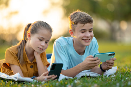 Teenagers boy and girl playing video games on their cellphones outdoors sitting in summer park.の写真素材