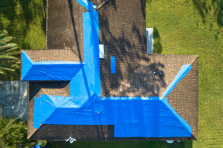 Top view of leaking house roof covered with protective tarp sheets against rain water leaks until replacement of asphalt shingles. Damage of building rooftop as aftermath of hurricane Ian in Floridaの写真素材