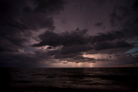 Thunderstorm dark clouds with lightning and thunder over evening sea water waves crushing on sandy...