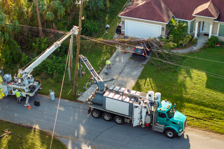 Utility services fixing damaged power lines after hurricane in Florida. Workers using bucket trucks to repair blown down electrical wires at residential homeの写真素材
