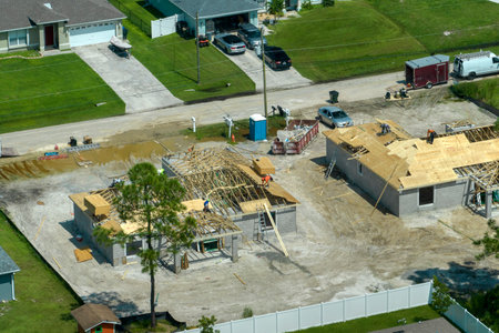 Aerial view of builders working on unfinished residential house with wooden roof frame structure under construction in Florida suburban areaの写真素材