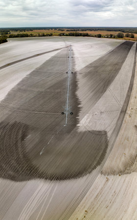 Industrial sprinkler spraying water on farmland ground for crops growth during period of drought. Irrigation system watering farm field during dry seasonの写真素材