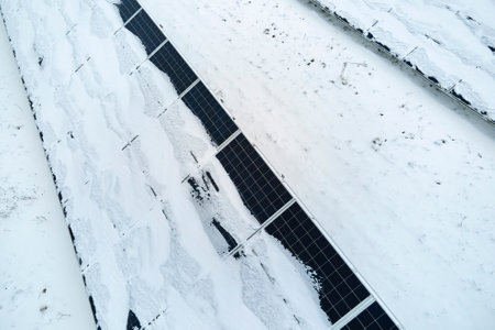 Aerial view of snow melting from covered solar photovoltaic panels at sustainable electric power...
