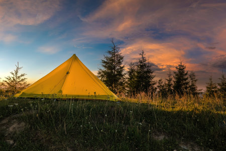 Sunset mountain landscape with tourist camping tent on hillside campsite at bright sunny evening. Active tourism and hiking conceptの写真素材