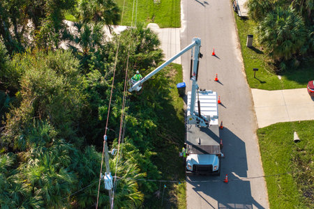 Maintenance of electrical grid by city utility cervices. Worker in lift truck trimming tree around power linesの写真素材