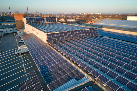 Aerial view of blue photovoltaic solar panels mounted on industrial building roof for producing...