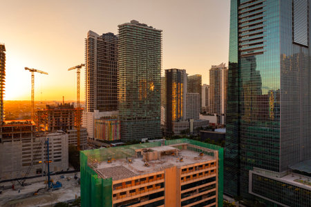 Housing growth in the USA. New skyscraper construction in Miami, Florida at sunset. Developing residence in American urban area. Industrial tower lifting cranes at building site.の写真素材