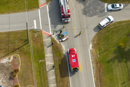 Victim of car accident on medical stretcher. First responders responding to car hit cyclist on street. Emergency medical technicians helping person of vehicle hitting pedestrian on road in USAの写真素材