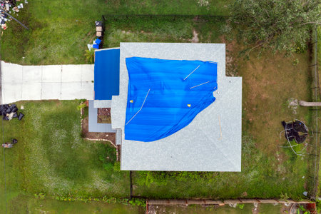 Aerial view of damaged in hurricane house roof covered with blue protective tarp against rain water leaking until replacement of asphalt shinglesの写真素材