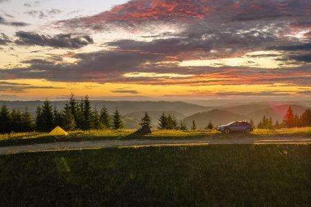 Offroad camping site on hillside at bright sunset. SUV vehicle and tent shelters on mountain campsite on sunny evening. Active tourism and hiking conceptの写真素材