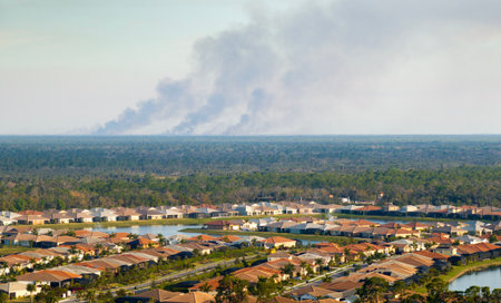 Toxic smoke from prescribed forest fire rising up over suburban neighborhood in Florida polluting airの写真素材