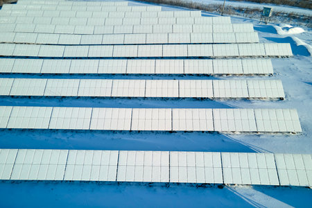 Aerial view of snow covered sustainable electric power plant with rows of solar photovoltaic panels...