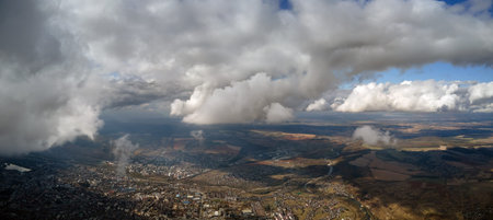 Aerial view from airplane window at high altitude of distant city covered with white puffy cumulus...