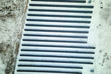 Aerial view of snow melting from covered solar photovoltaic panels at sustainable electric power...