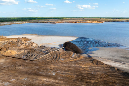 Mining equipment pumping water and sand through metal pipe at open phosphate pit in central Florida.
