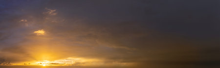 Colorful sunset sky with setting sun behind vivid orange and yellow clouds