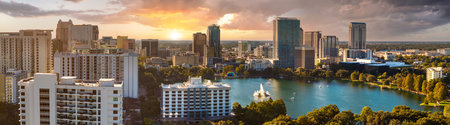 Panoramic aerial view of downtown Orlando overlooking Lake Eola at sunset. Glass office towers contrast with green park and scenic waterfront.