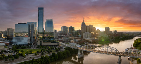 Urban landscape of downtown Nashville in Tennessee, USA at sunset. Tall skyscrapers with scenic waterfront skyline and bridge in evening haze.