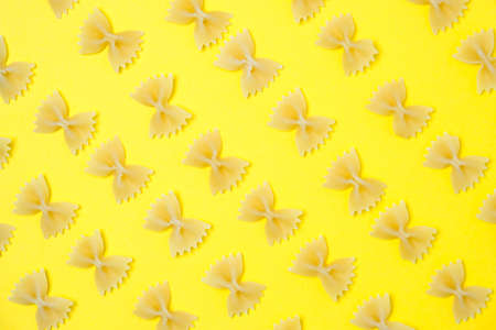 Close up pattern of noodles farfalle also known as bow-tie or butterfly pasta placed on yellow...