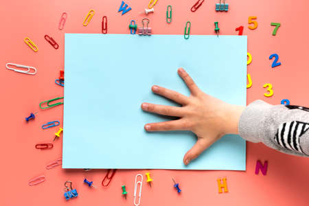 Many colorful letters and paper clips and child hand on blue and pink paper background.の写真素材