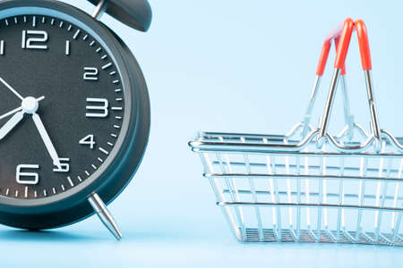 Black vintage analog alarm clock and small shopping basket on blue background.の写真素材